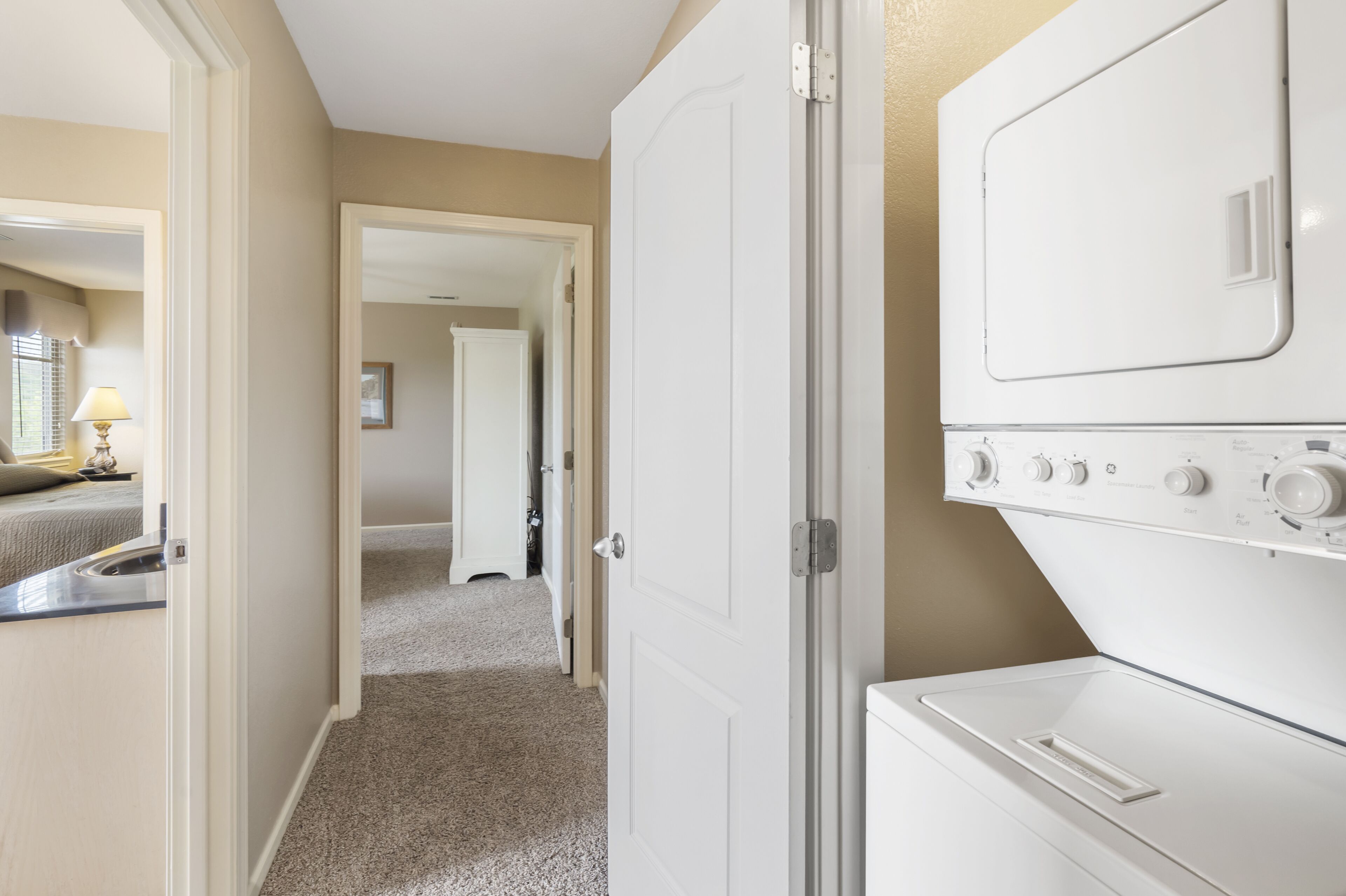 A laundry room with a washer and dryer, carpeted floor, and a hallway leading to another room.