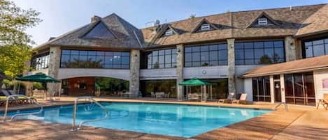 A large building with a swimming pool, outdoor seating, and a covered patio area.
