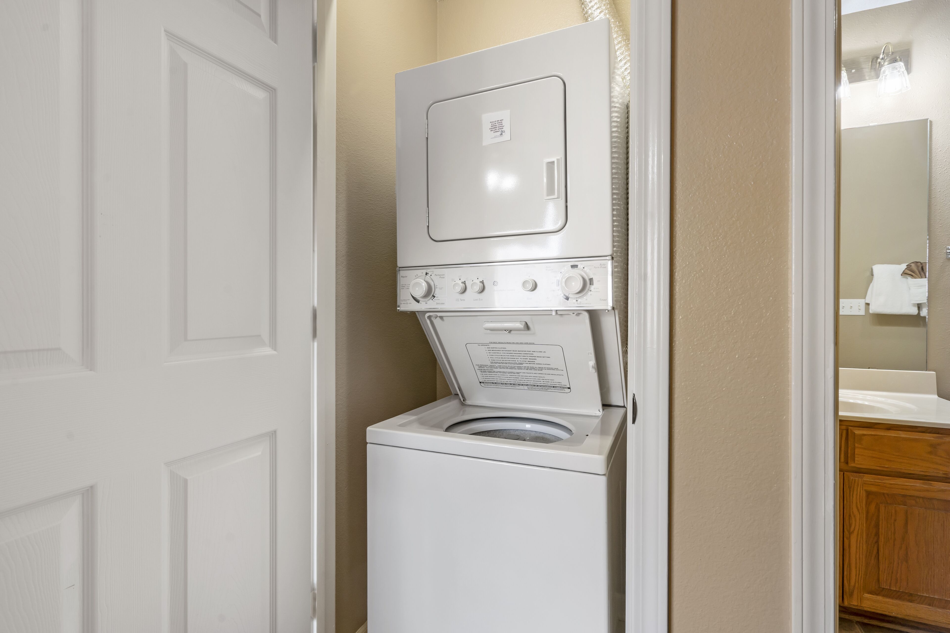 A compact washer and dryer unit in a bathroom with a wooden cabinet and a mirror.