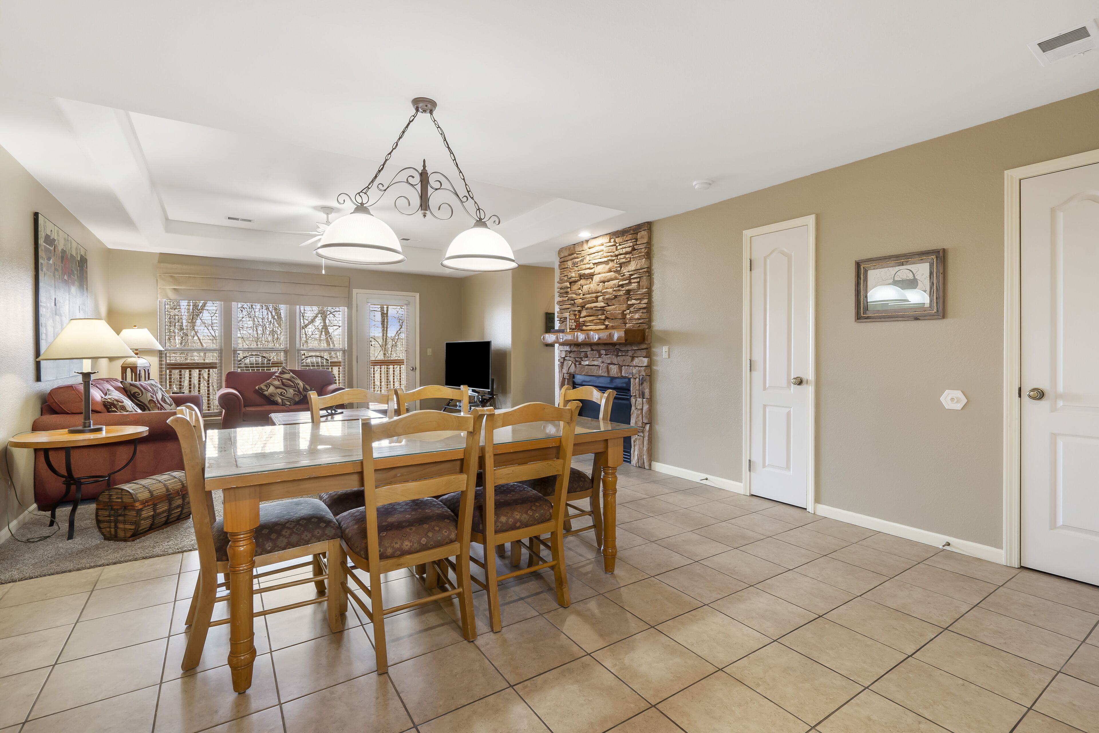 A spacious dining area with a wooden table and chairs, a chandelier, and a stone fireplace.
