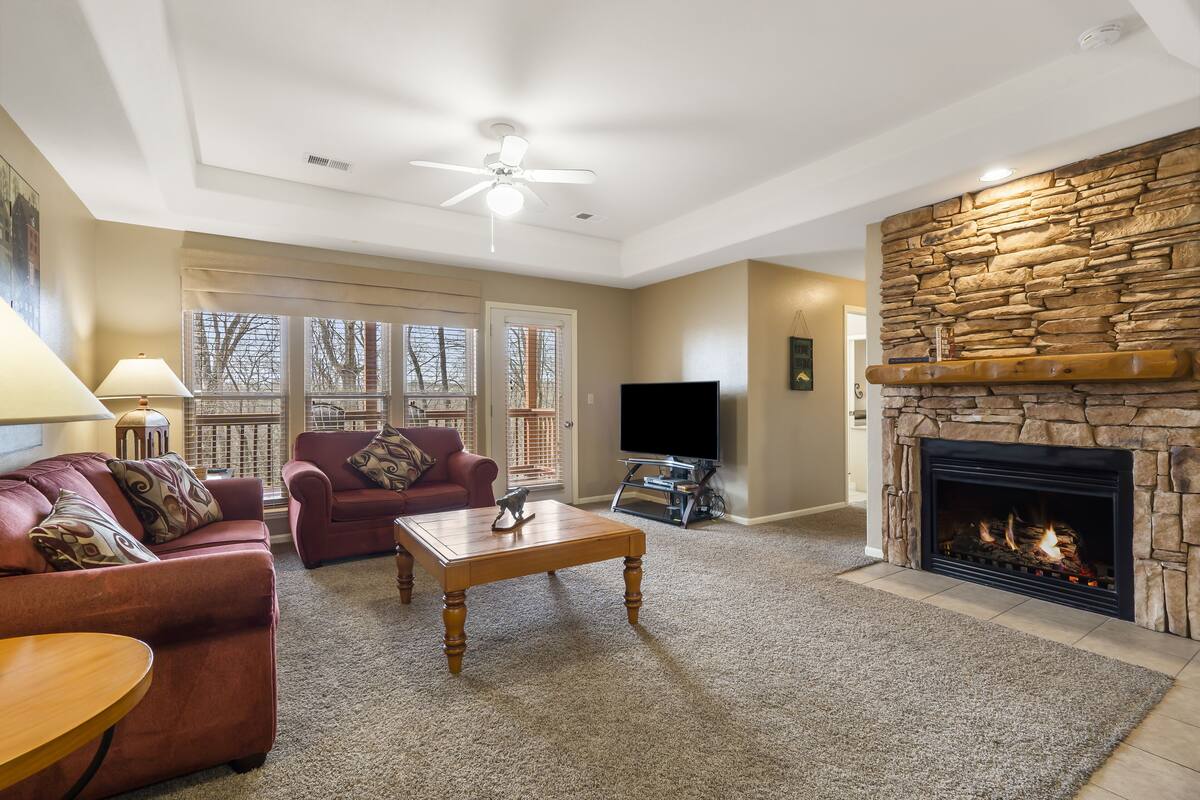 A living room with a stone fireplace, a ceiling fan, a television, and a red sofa.