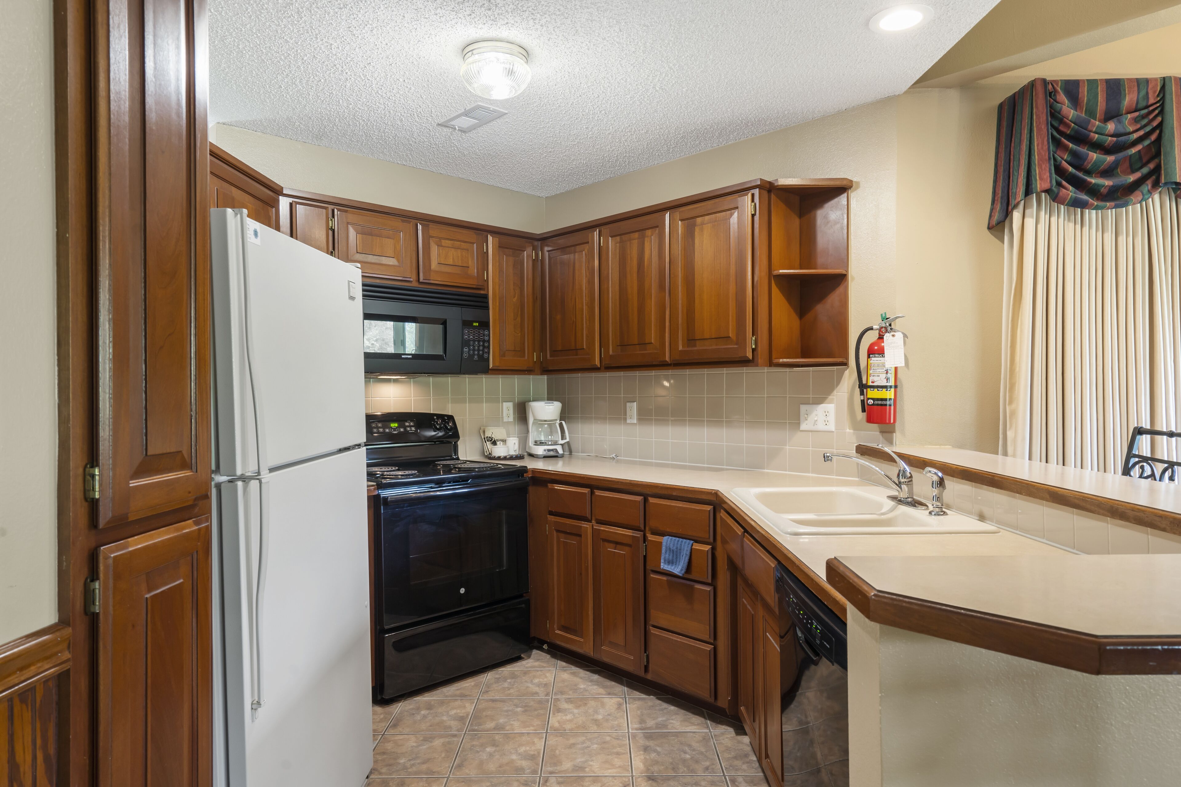 A kitchen with wooden cabinets, a refrigerator, a microwave, an oven, a coffee maker, and a sink.