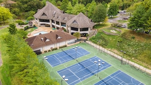 A tennis court complex with multiple courts, a building with a distinctive roof, and surrounding greenery. - Stonebridge Village Resort (Branson West)