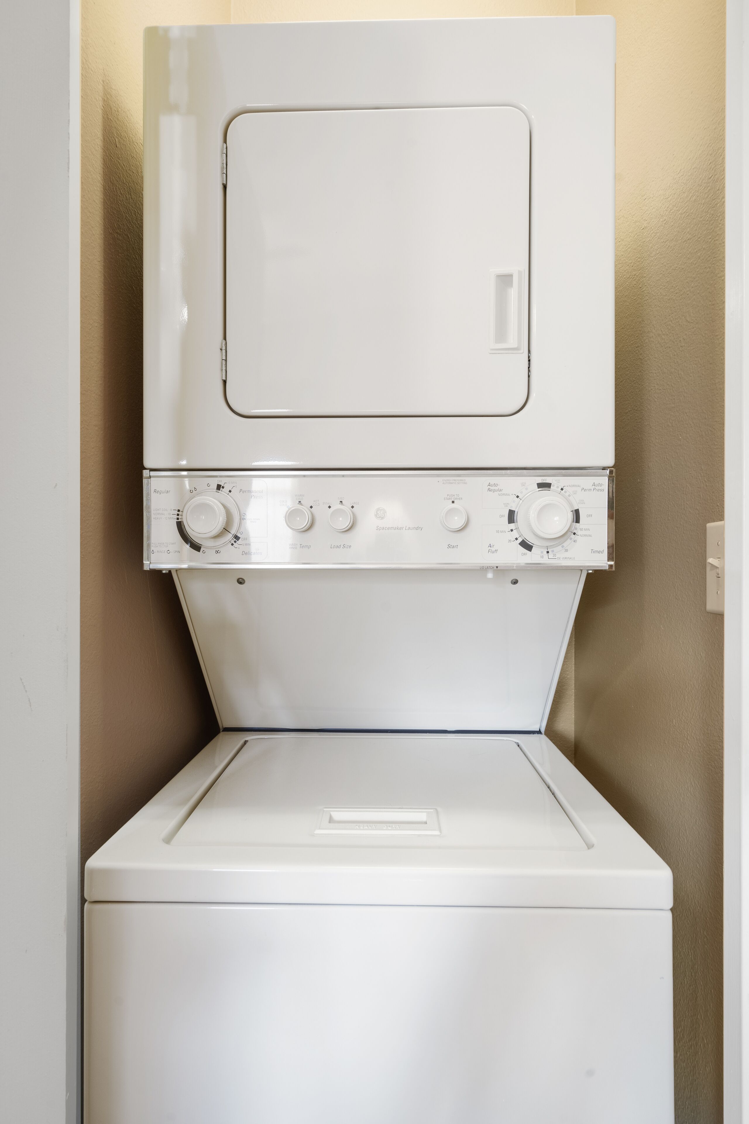 A white washing machine with control knobs and a door, mounted on a beige wall.