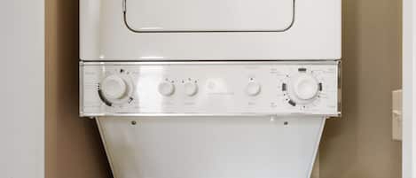 A white washing machine with control knobs and a door, mounted on a beige wall.