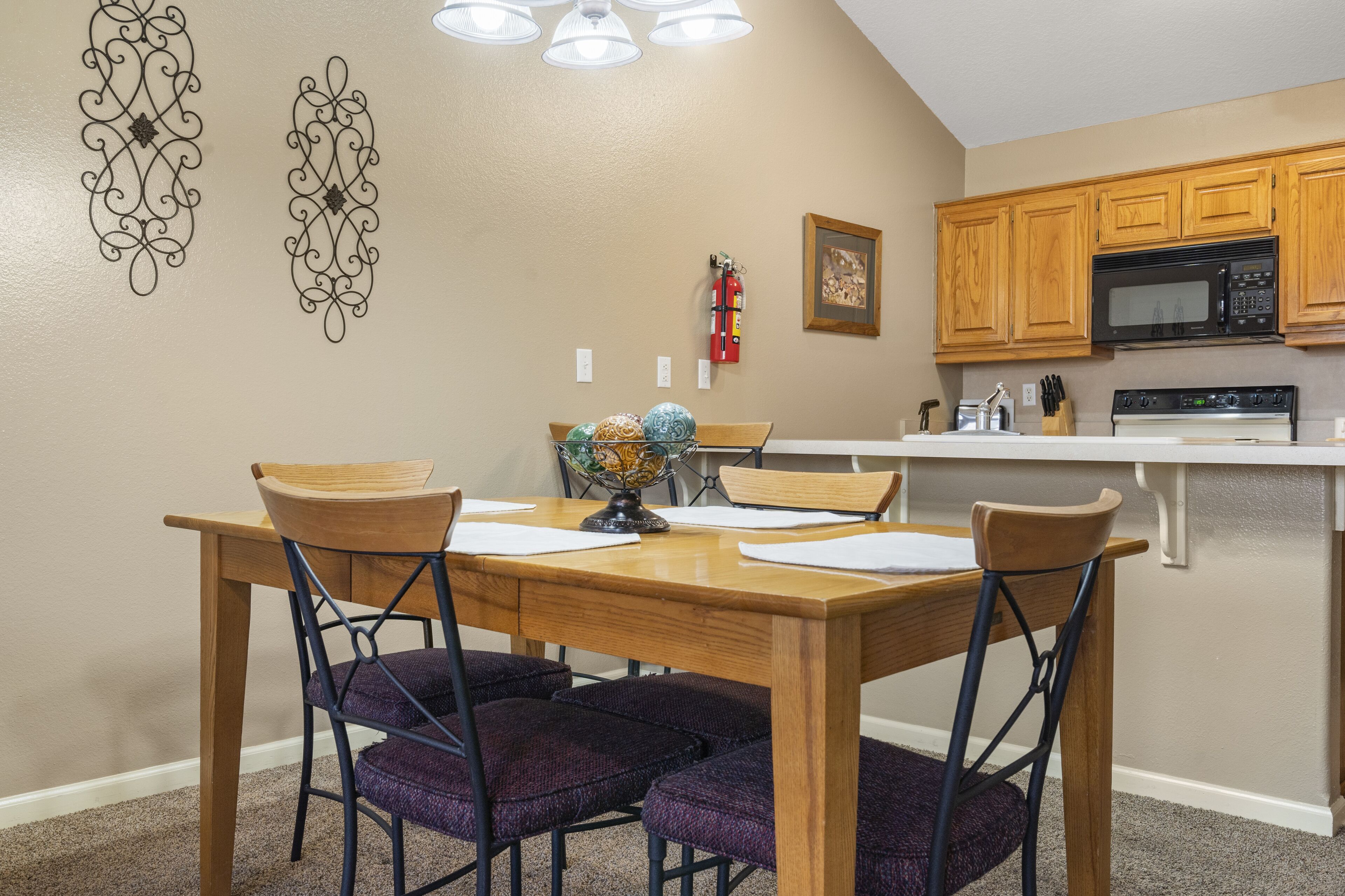 A dining area with a wooden table and chairs, a globe centerpiece, and a kitchen with wooden cabinets and a microwave.