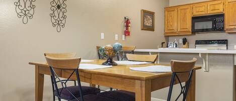 A dining area with a wooden table and chairs, a globe centerpiece, and a kitchen with wooden cabinets and a microwave.