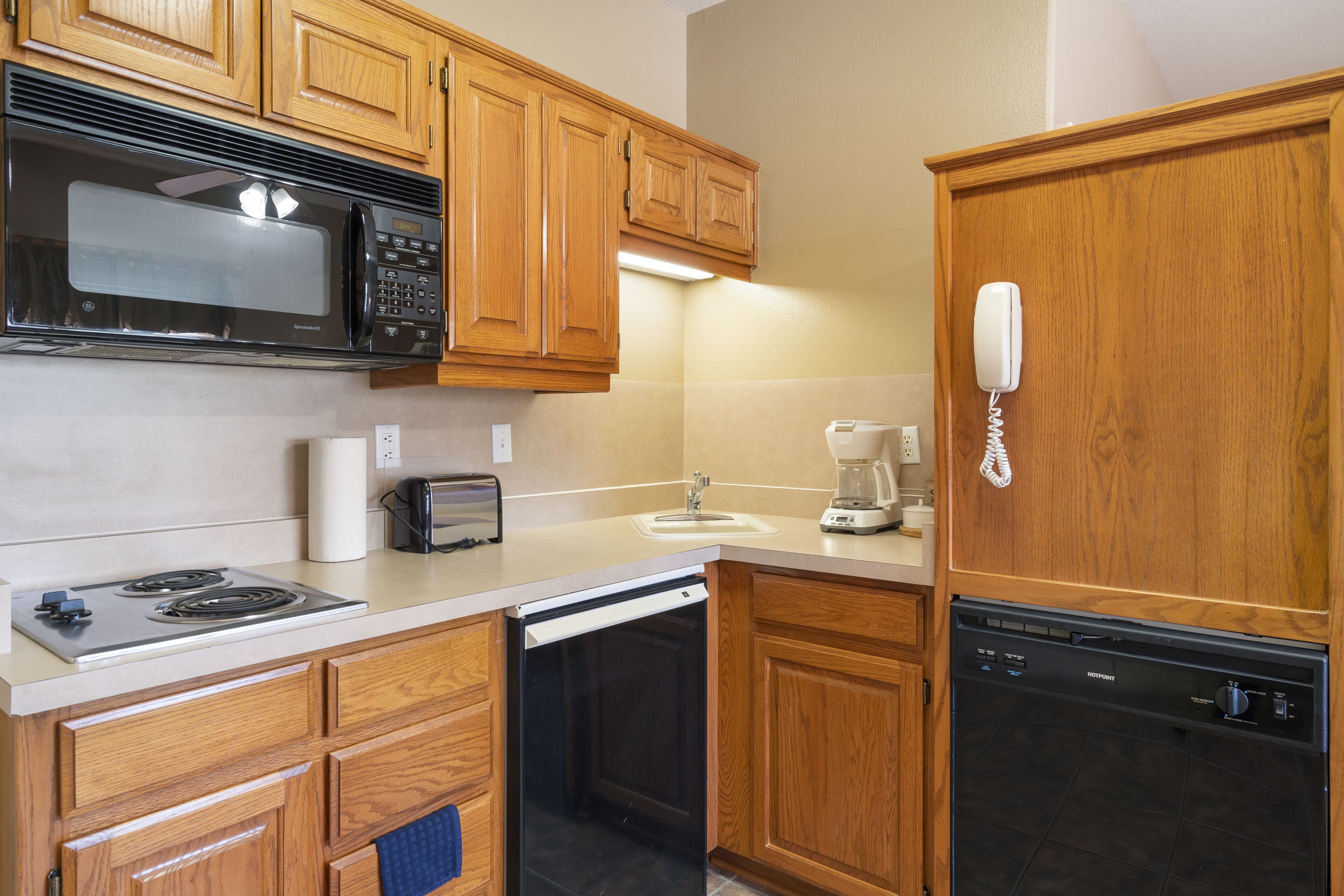 A kitchen with wooden cabinets, a microwave, a toaster, a coffee maker, a dishwasher, and a phone.