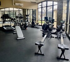 A gym with various exercise equipment, large windows, and a stone wall.