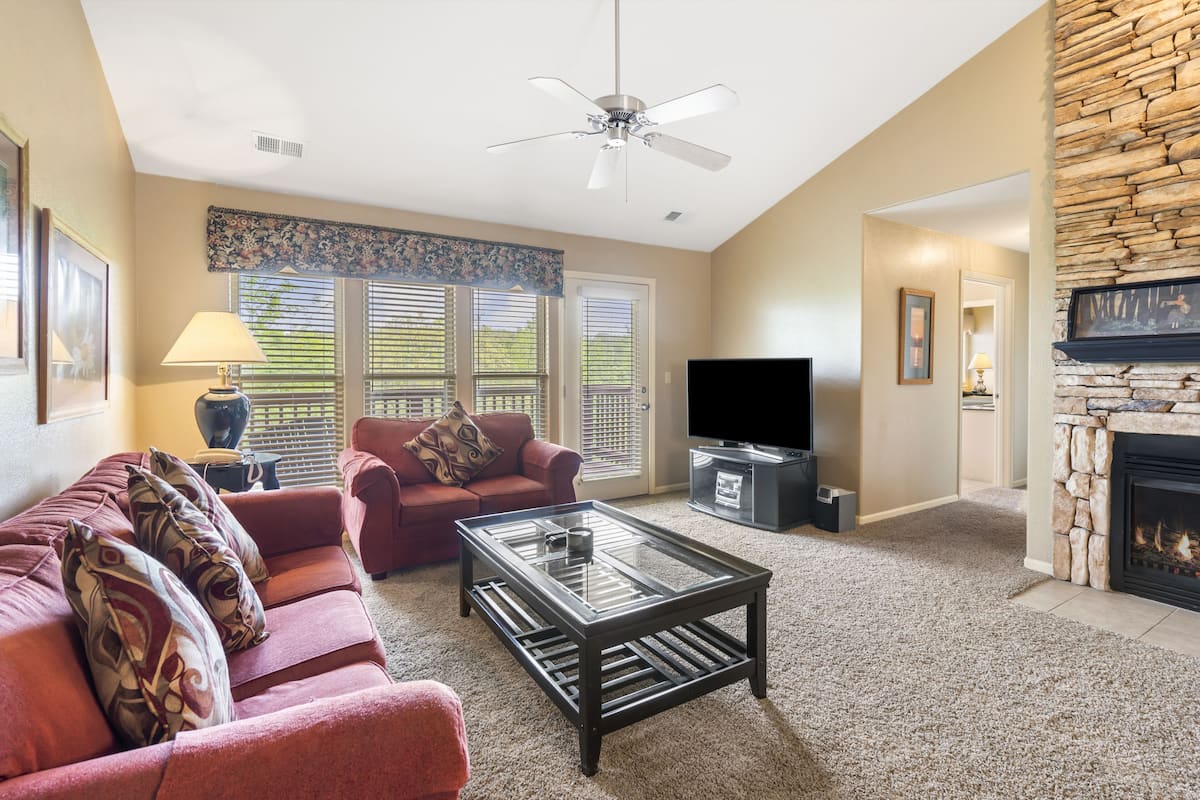 A living room with a red sofa, a glass coffee table, a television, and a fireplace.
