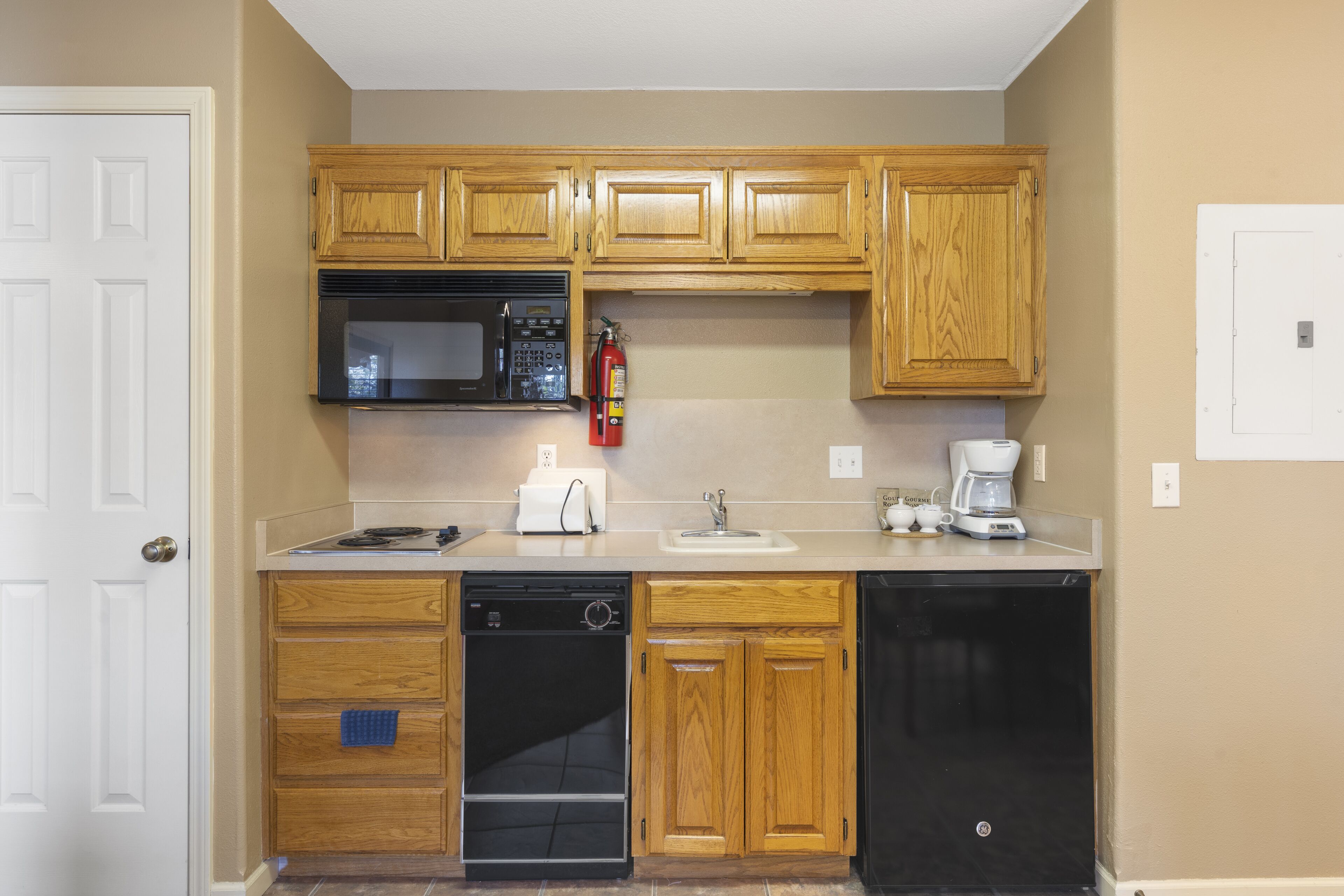 Una cocina compacta con armarios de madera, microondas, lavavajillas y cafetera.