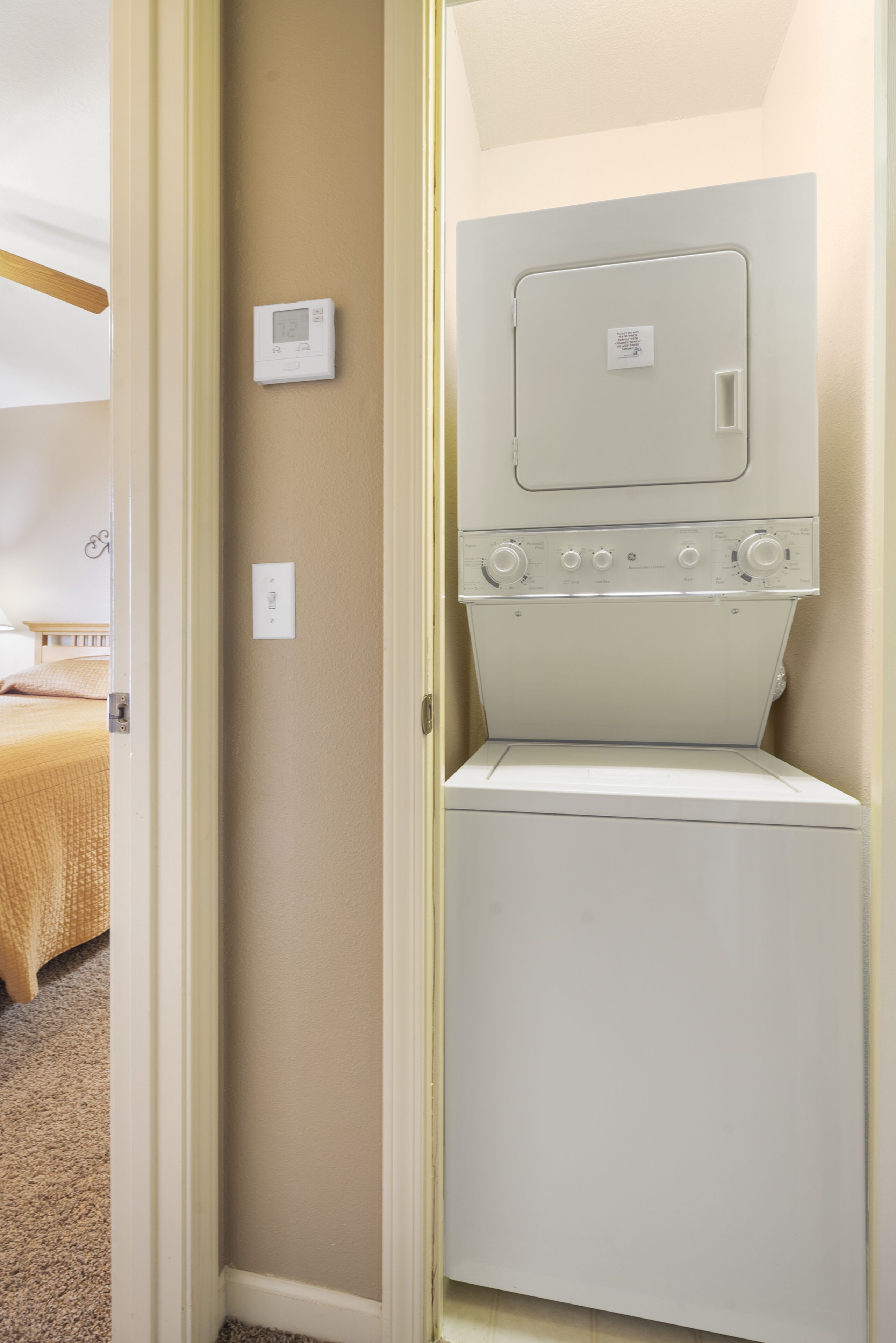 A laundry room with a front-loading washer and dryer, a thermostat, and a door with a sign.