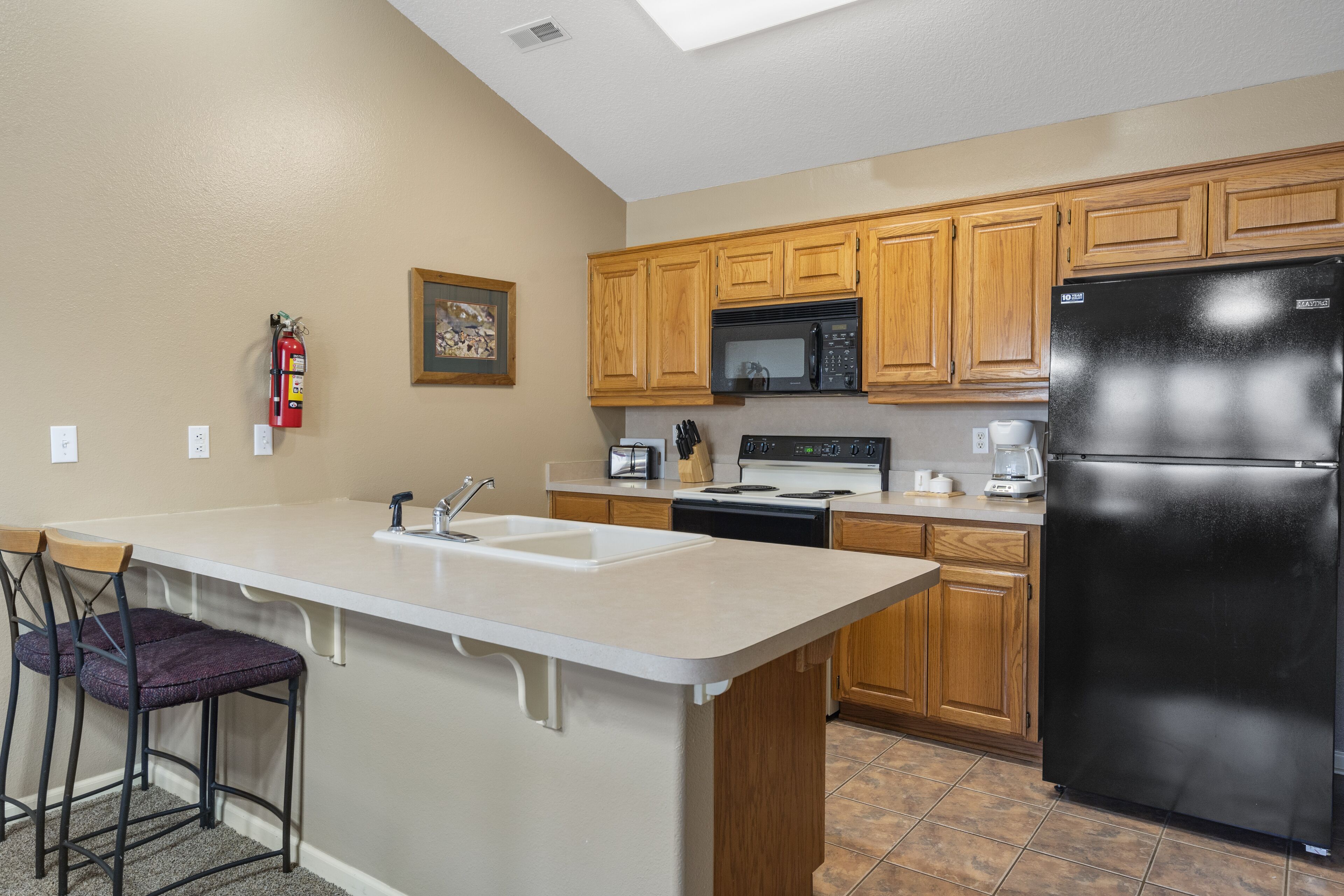 A kitchen with wooden cabinets, a black refrigerator, a microwave, and a sink.
