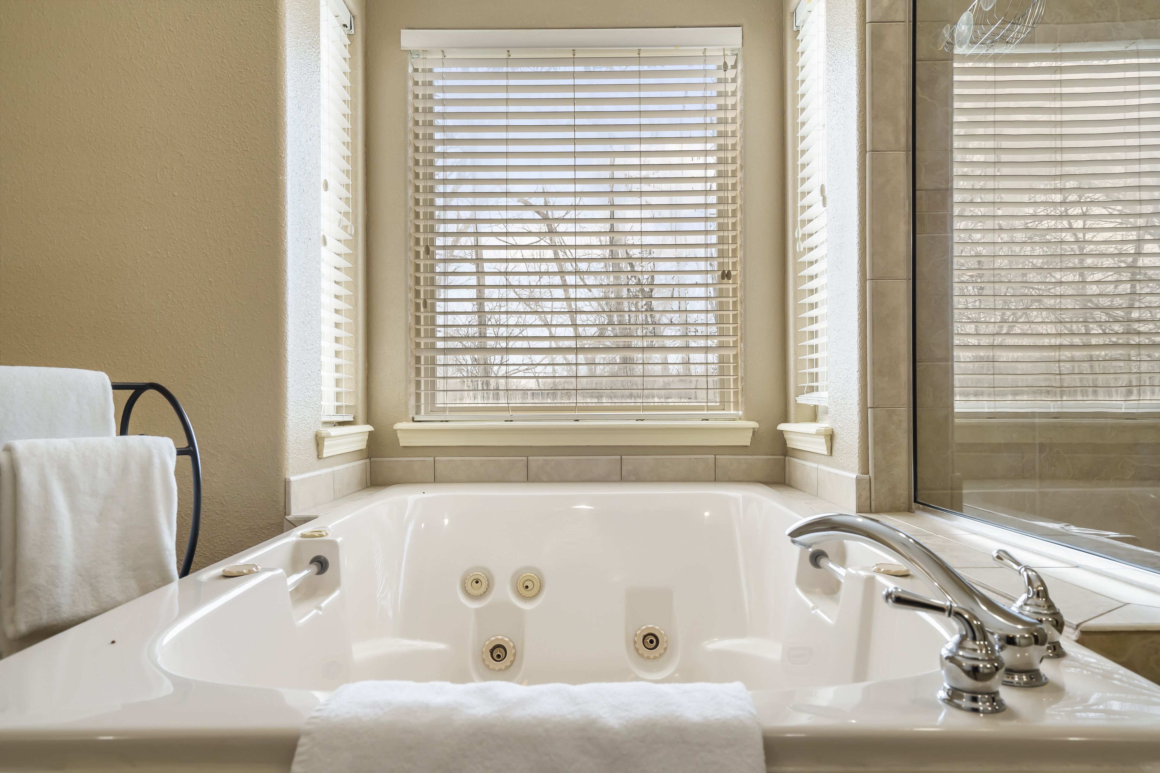 Une salle de bain avec une grande baignoire, une fenêtre avec des stores et une serviette à proximité.