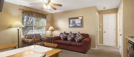 A living room with a red sofa, a wooden dining table, and a ceiling fan.