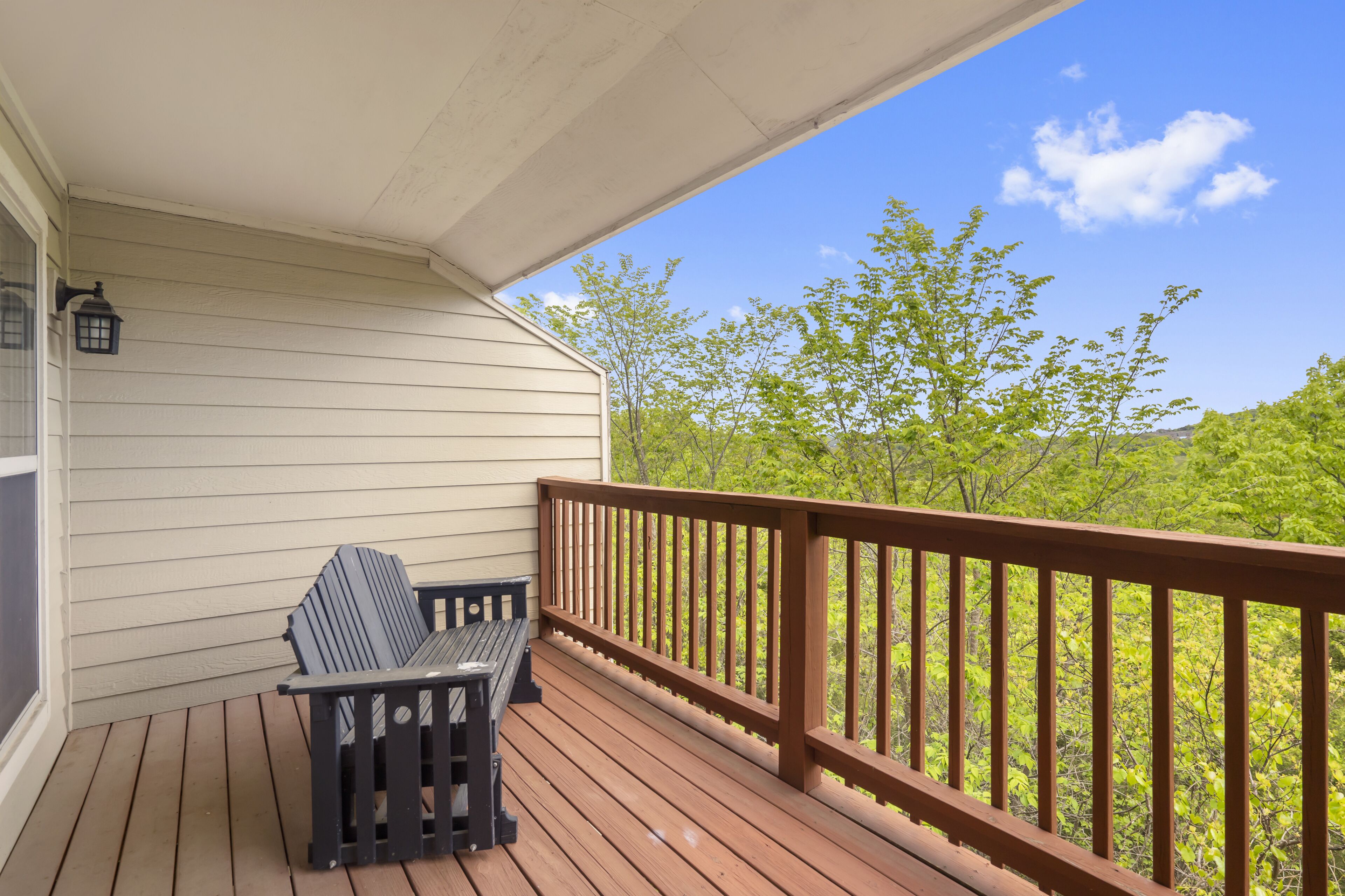 A wooden deck with a bench and a table, overlooking a forested area.