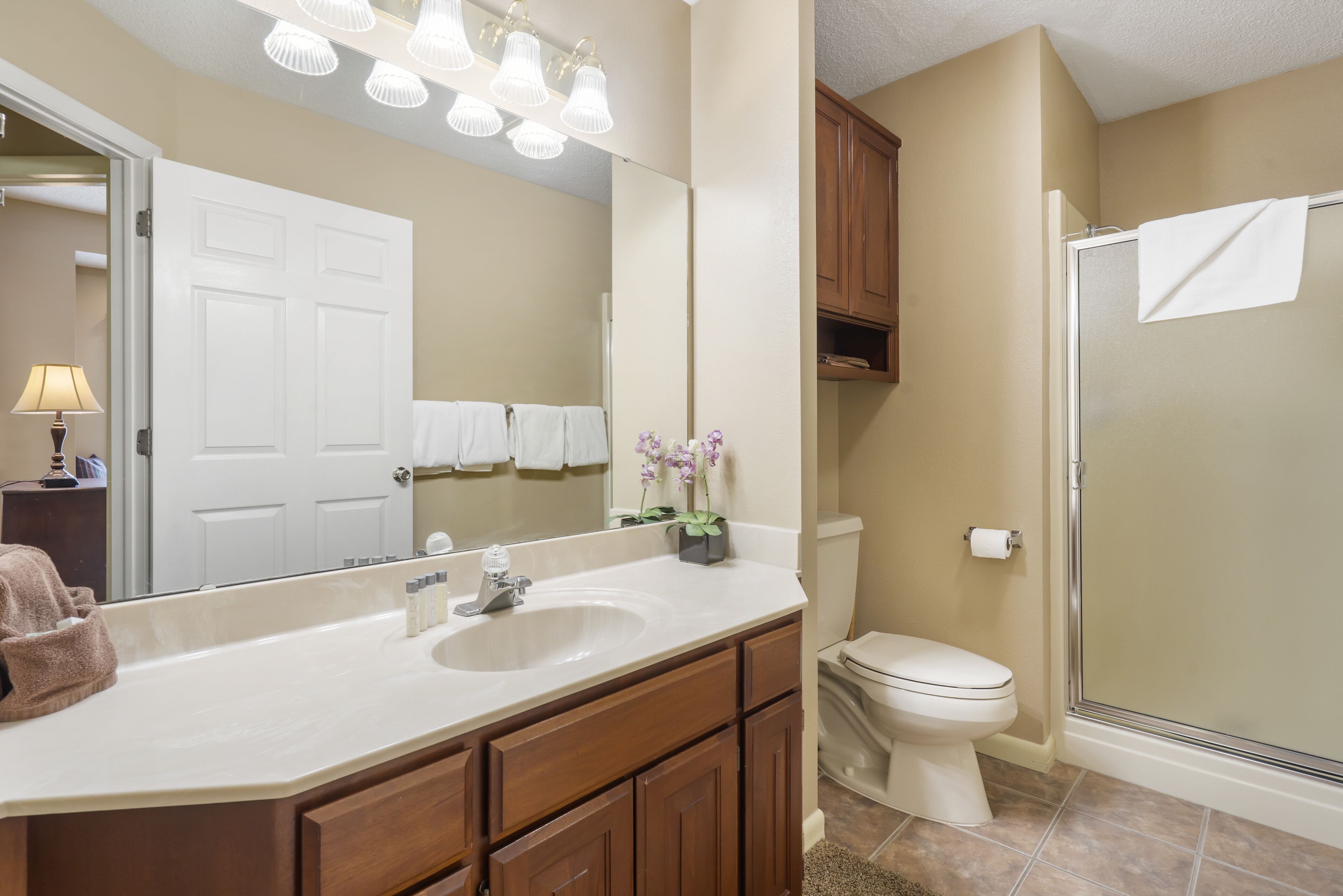 A bathroom with a white sink, wooden cabinets, a toilet, and a glass-enclosed shower.
