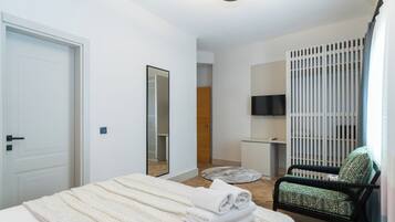Quarto moderno com uma cama, uma poltrona, uma televisão e um espelho.