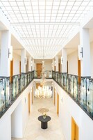 Un amplio pasillo de hotel con barandilla de vidrio, un candelabro y una mesa redonda central.