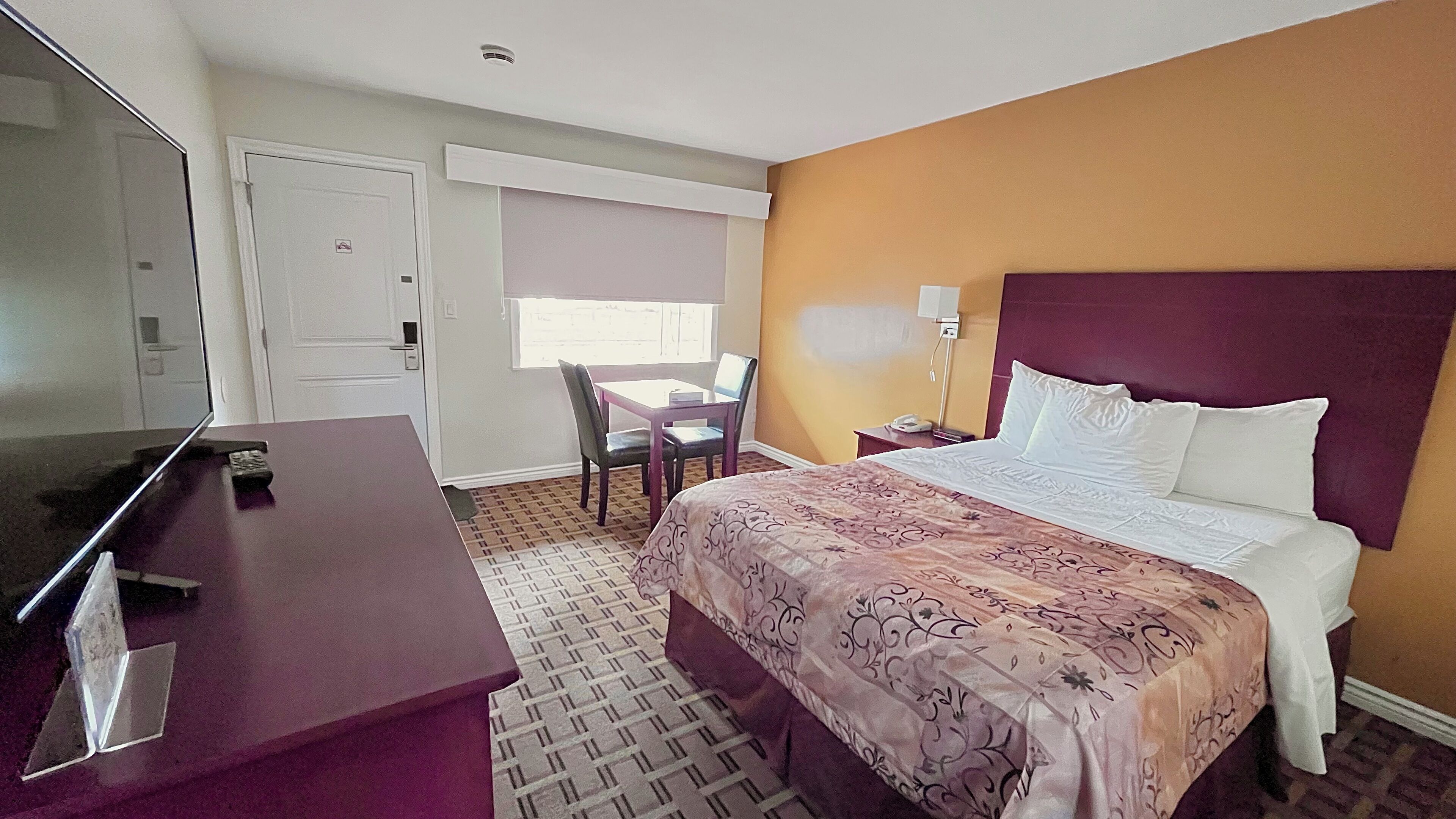A hotel room with a bed, a desk, a chair, a TV, and a window.