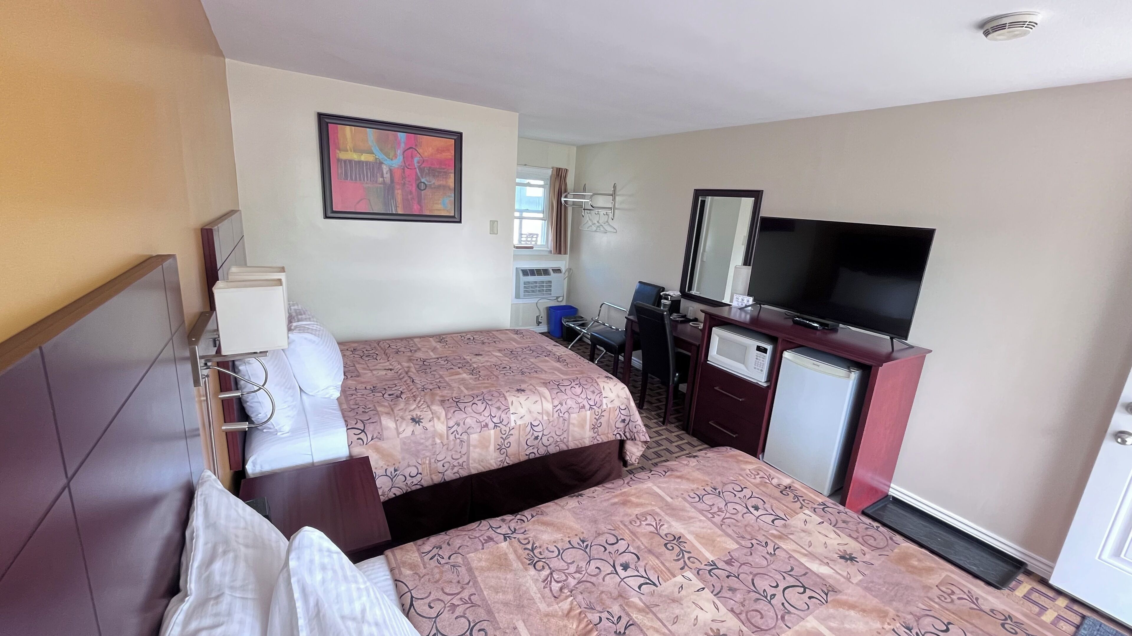 A hotel room with two beds, a desk with a chair, a television, a microwave, and a small refrigerator.