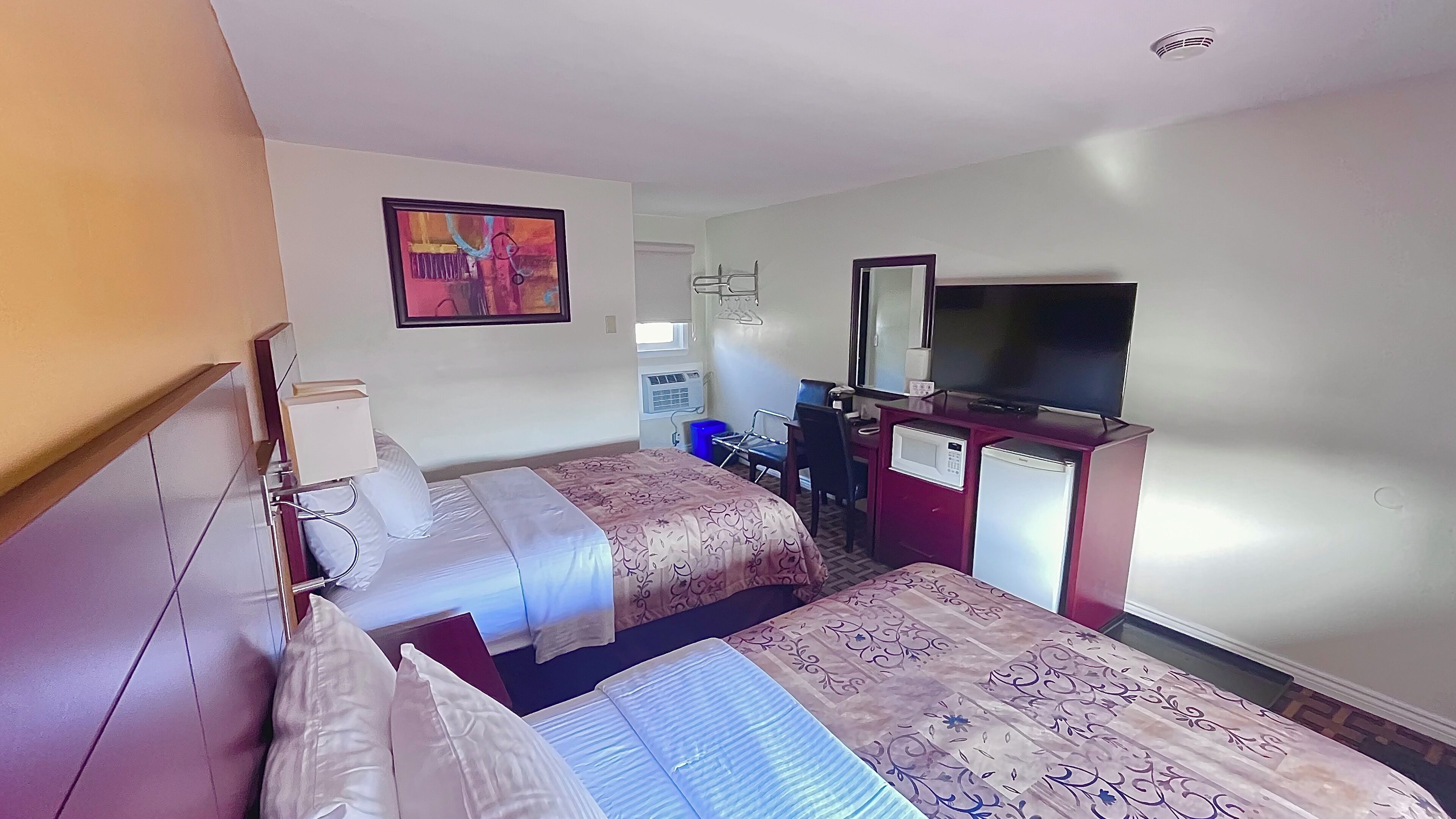 Habitación de hotel con dos camas, un televisor, un escritorio con microondas y una ventana con aire acondicionado.