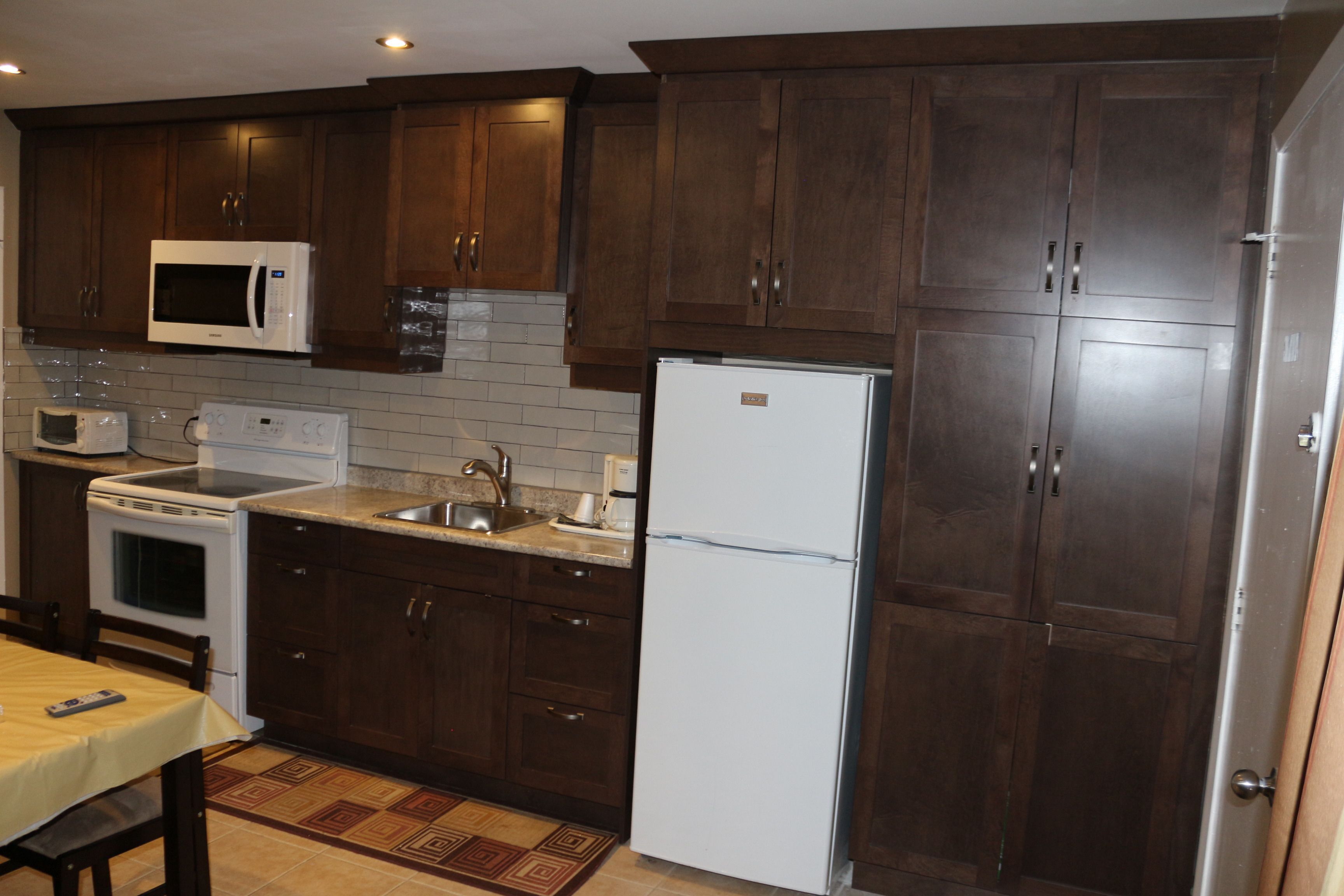 Una cocina con alacenas de madera oscura, un refrigerador blanco, un microondas, una estufa y un lavamanos.