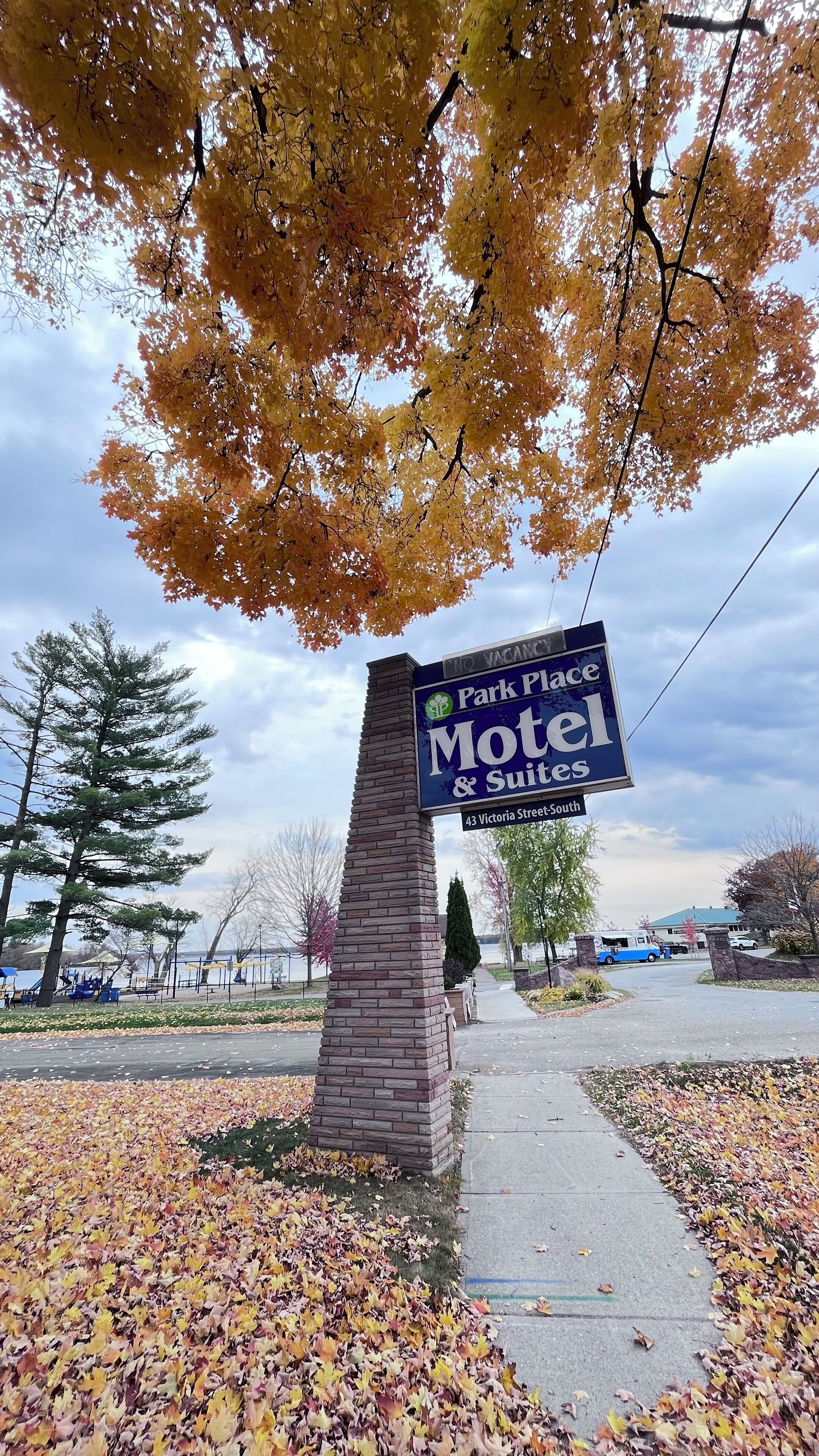 A motel sign with a brick pillar, surrounded by autumn leaves.
