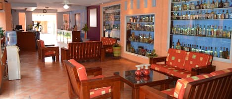 A lobby with wooden furniture, a water dispenser, and a bar area with shelves of bottles.