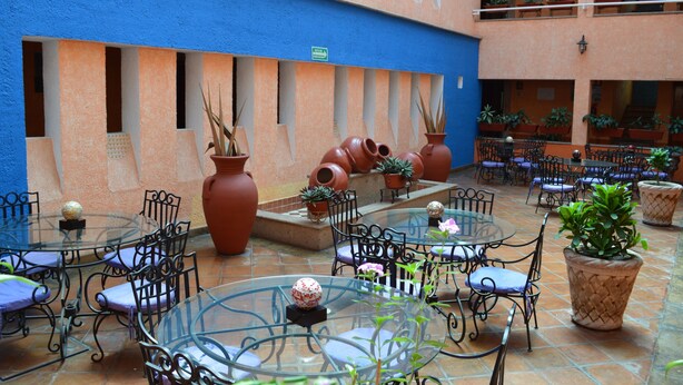 An outdoor patio area with round glass tables and metal chairs, surrounded by terracotta pots and potted plants. - Hotel La Rienda Misión Tequillan (Tequila)