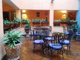 Un patio al aire libre con suelo de baldosas, varias mesas y sillas, y plantas en macetas.