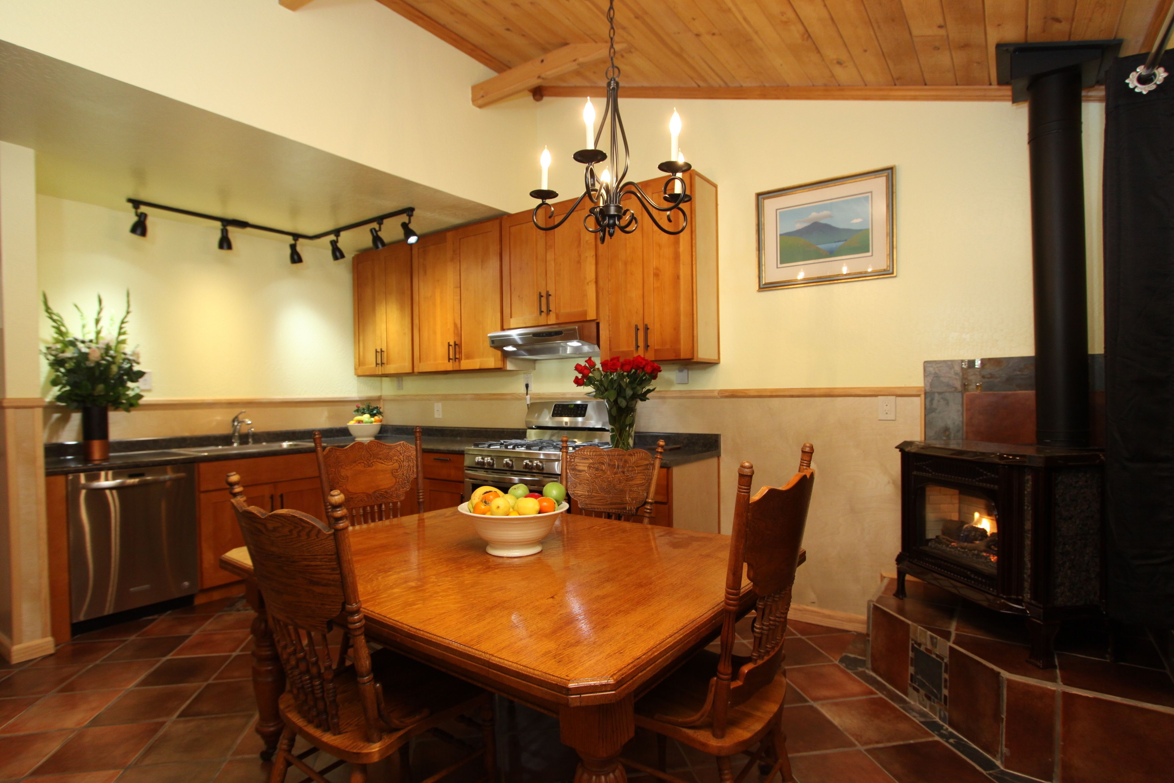A kitchen with wooden cabinets, a dining table with chairs, a chandelier, a stove, and a fireplace.