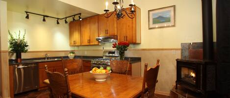 A kitchen with wooden cabinets, a dining table with chairs, a chandelier, a stove, and a fireplace.
