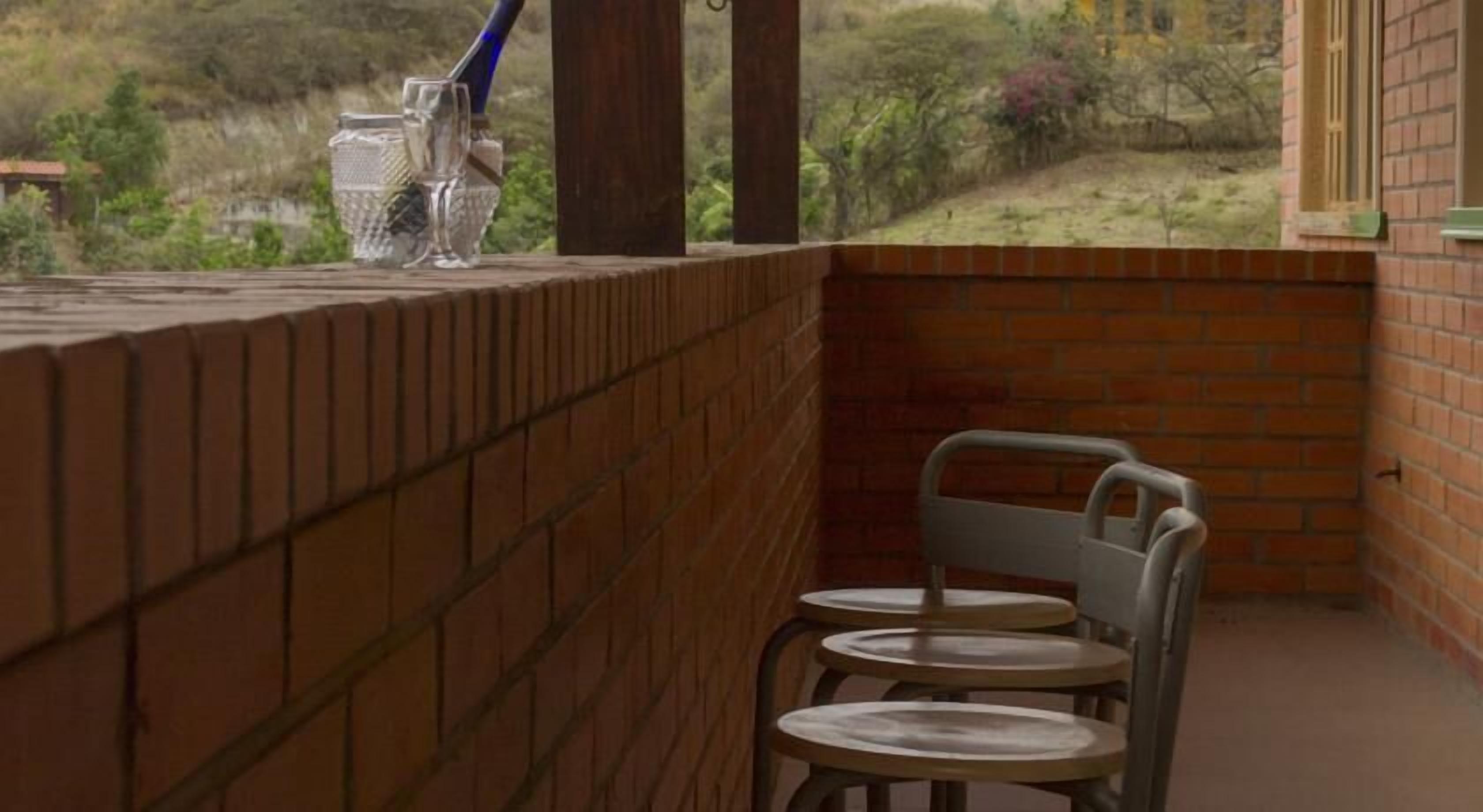 A balcony with a brick wall, a metal chair, and a glass table.