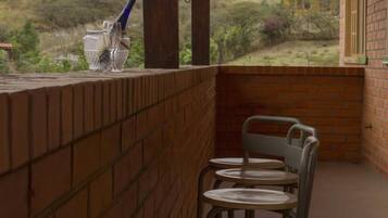 A balcony with a brick wall, a metal chair, and a glass table.