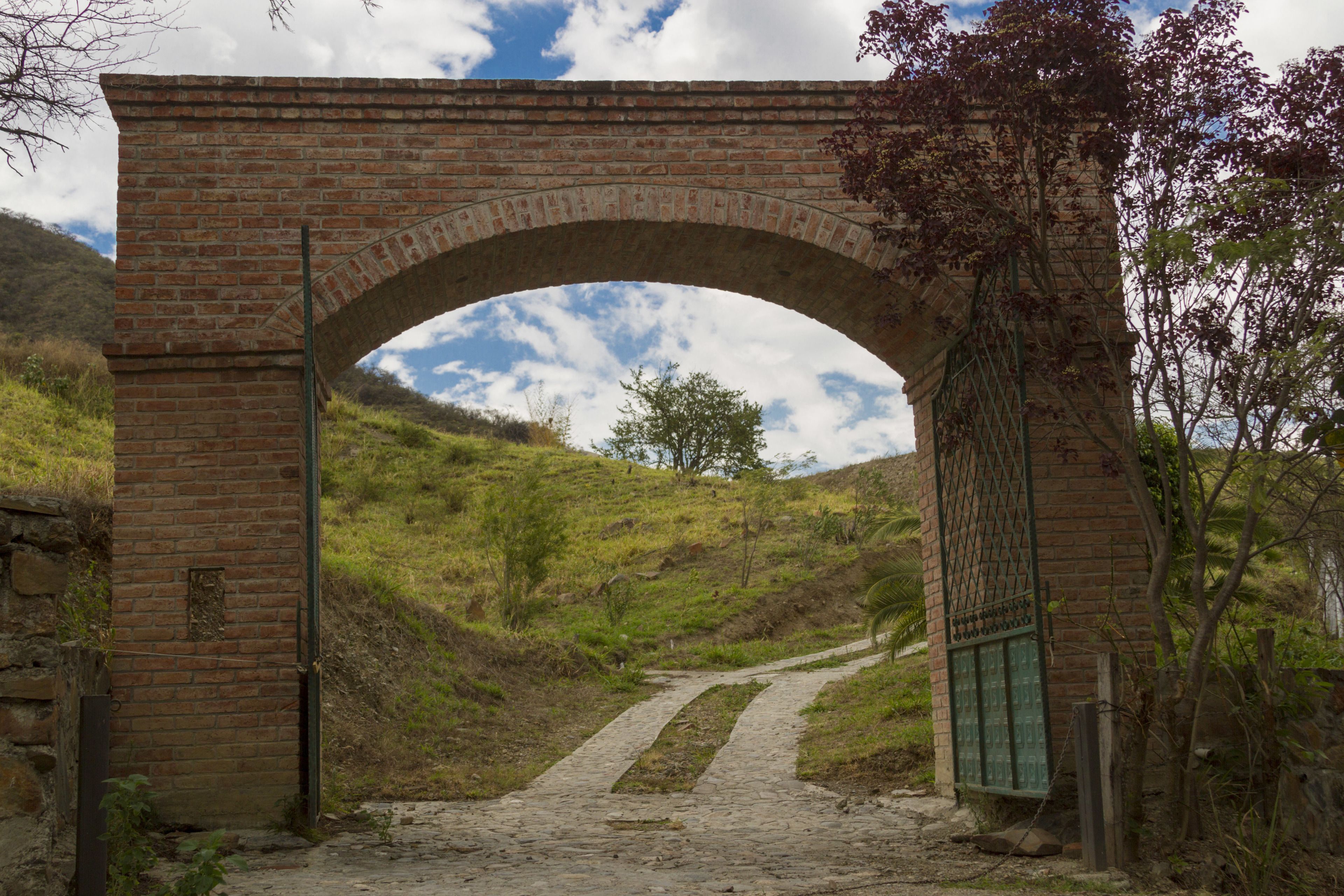 Un arco de ladrillo sobre un sendero de tierra, con una verja a la derecha.