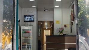 The entrance to Hotel Guanabara with a reception desk, a television screen, and a refrigerator with beverages. - Hotel Guanabara (Belo Horizonte)