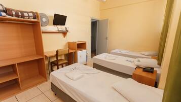 Quarto de hotel com duas camas de solteiro, uma escrivaninha com cadeira, um frigorífico pequeno e uma televisão na parede.