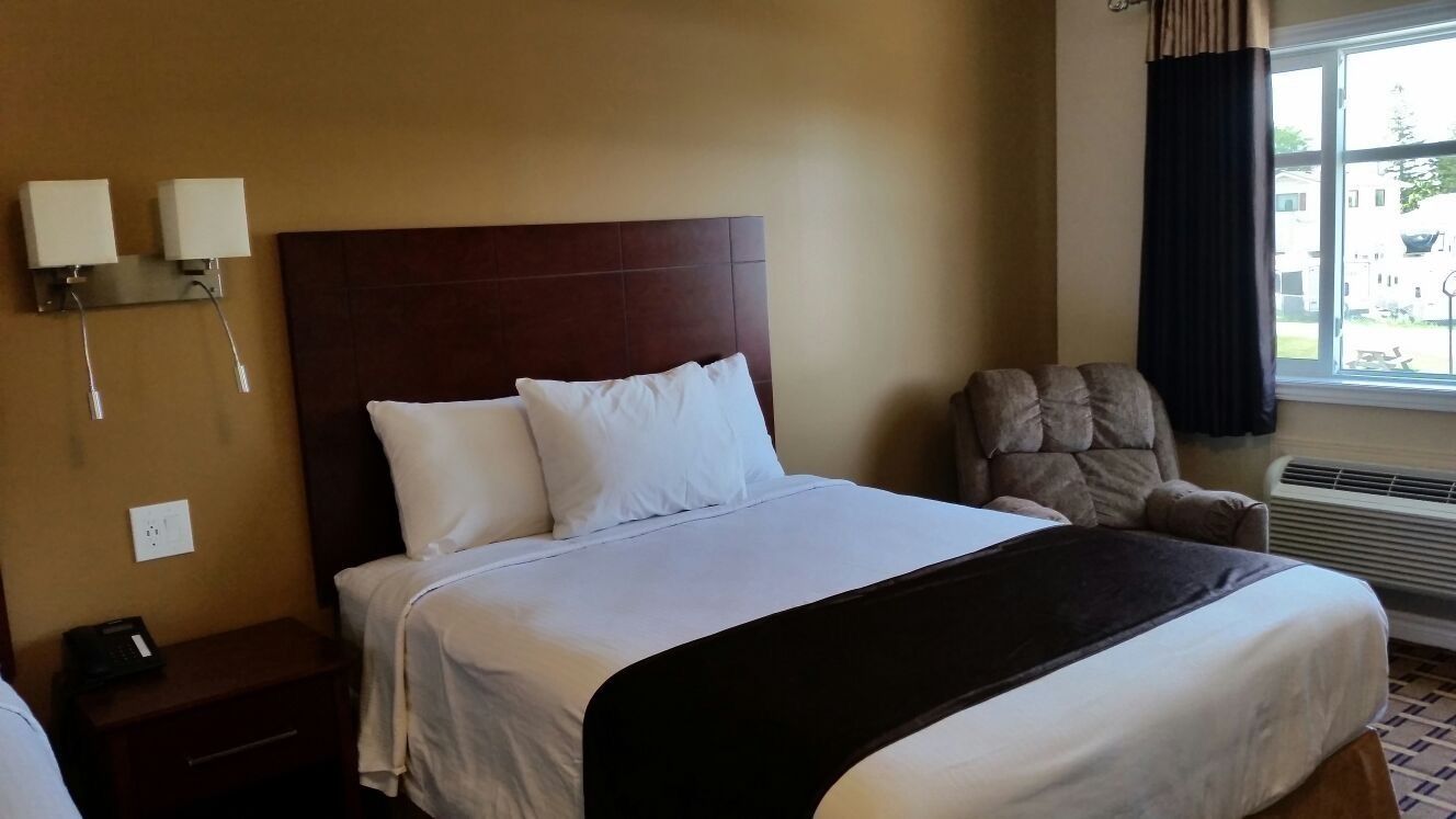A hotel room with a large bed, a chair, a nightstand, and a window with curtains.