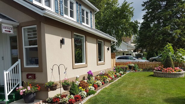 Une maison à deux étages avec un porche à l’avant, une boîte aux lettres et une pelouse bien entretenue agrémentée de parterres de fleurs.