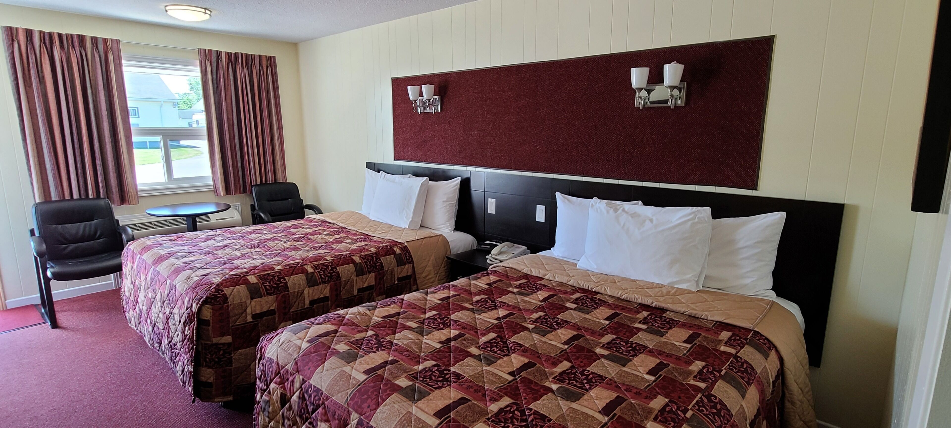 A hotel room with two beds, a small table, a chair, and a window with curtains.