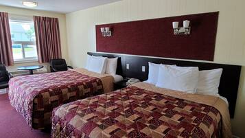 Una habitación de hotel con dos camas, una mesita, una silla y un ventanal con cortinas.