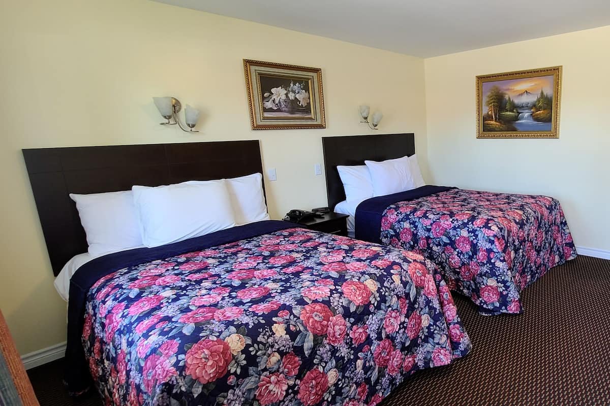 Ein Hotelzimmer mit zwei Betten, einem Schreibtisch mit Stuhl, einer Kaffeemaschine und Bildern an den Wänden.