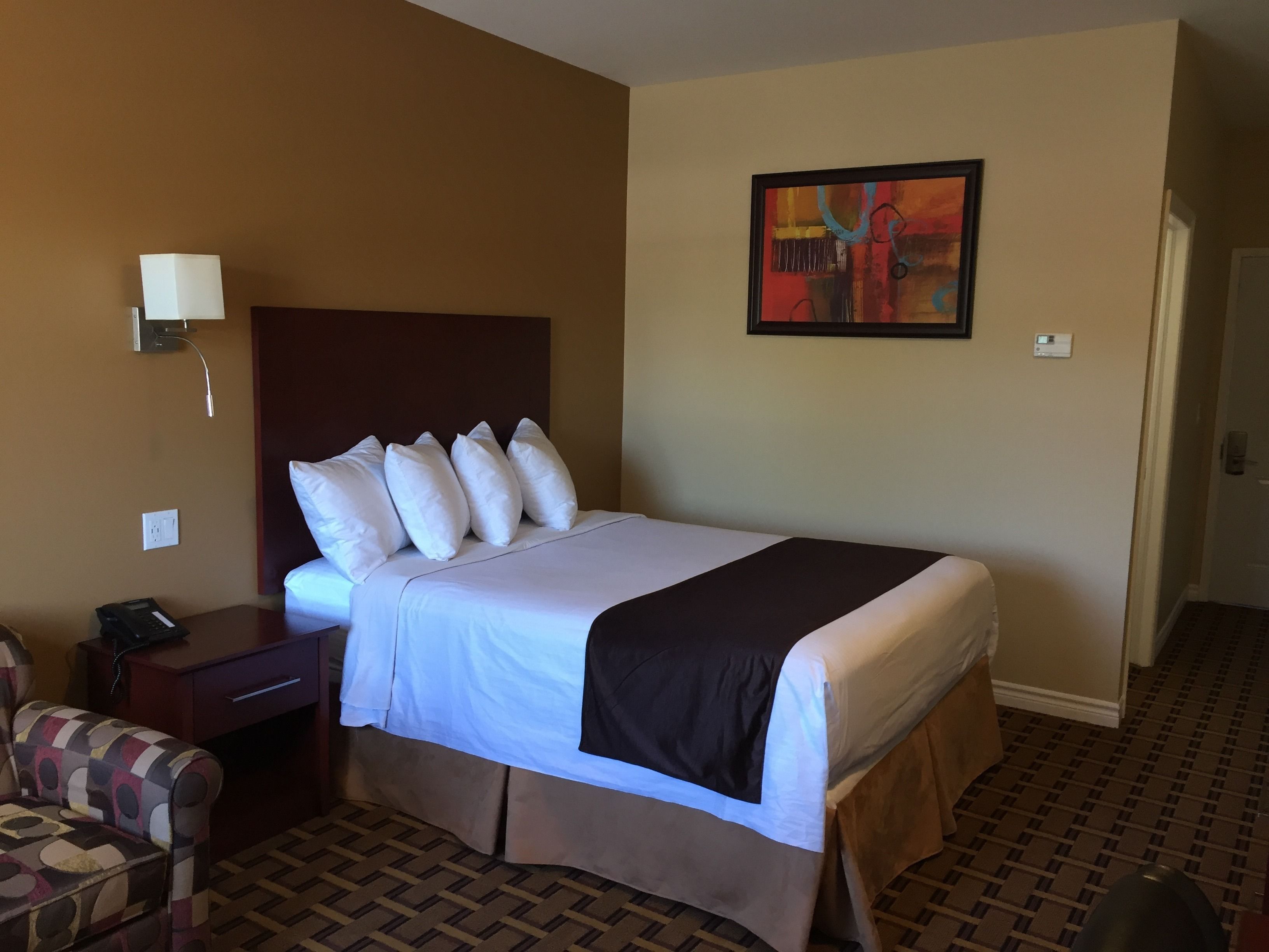 A hotel room with a bed, a nightstand, a chair, and a painting on the wall.