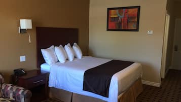 A hotel room with a bed, a nightstand, a chair, and a painting on the wall.