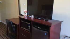 Une chambre d’hôtel équipée d’un bureau en bois, d’un téléviseur à écran plat, d’un four à micro-ondes, d’un réfrigérateur et d’une chaise.
