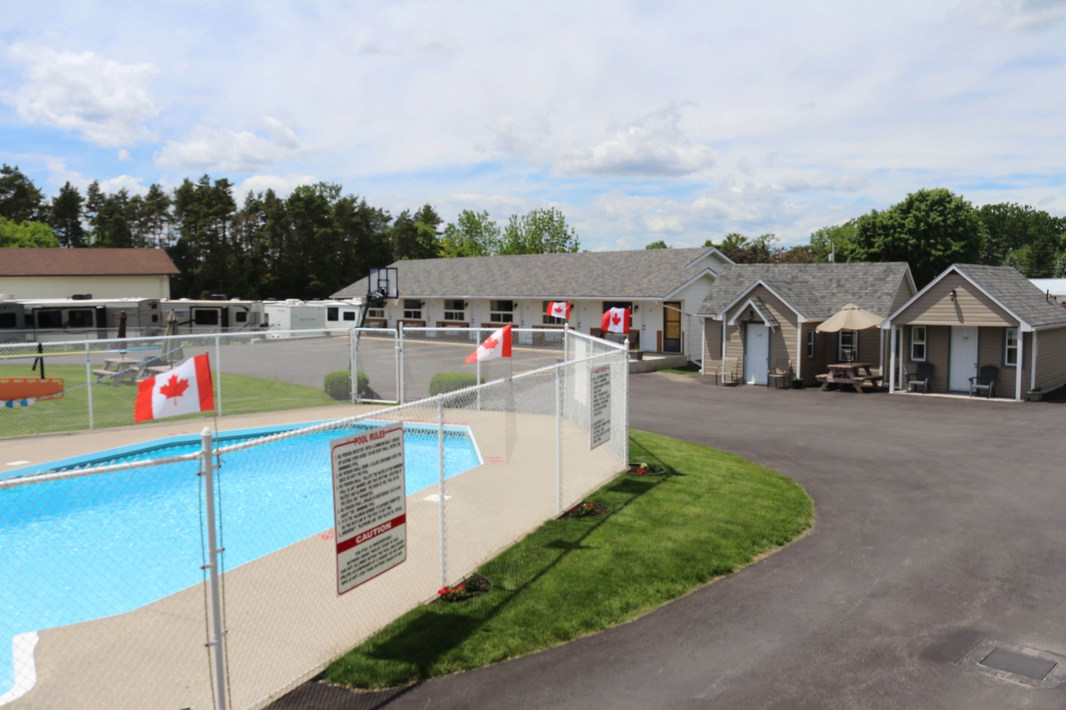 Un área de piscina con piscina cercada, banderas canadienses y un edificio con varias habitaciones.