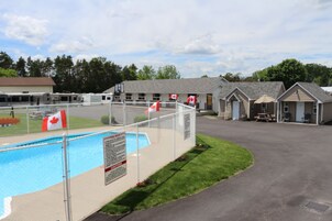 Un área de piscina con piscina cercada, banderas canadienses y un edificio con varias habitaciones.