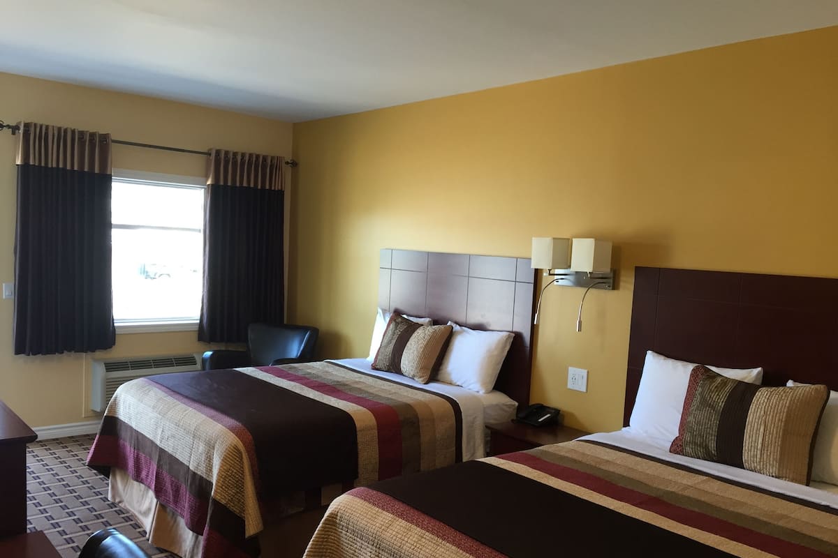 Ein Hotelzimmer mit zwei Betten, einem Schreibtisch, einem Stuhl, einem Fenster mit Vorhängen und einer Wandlampe.