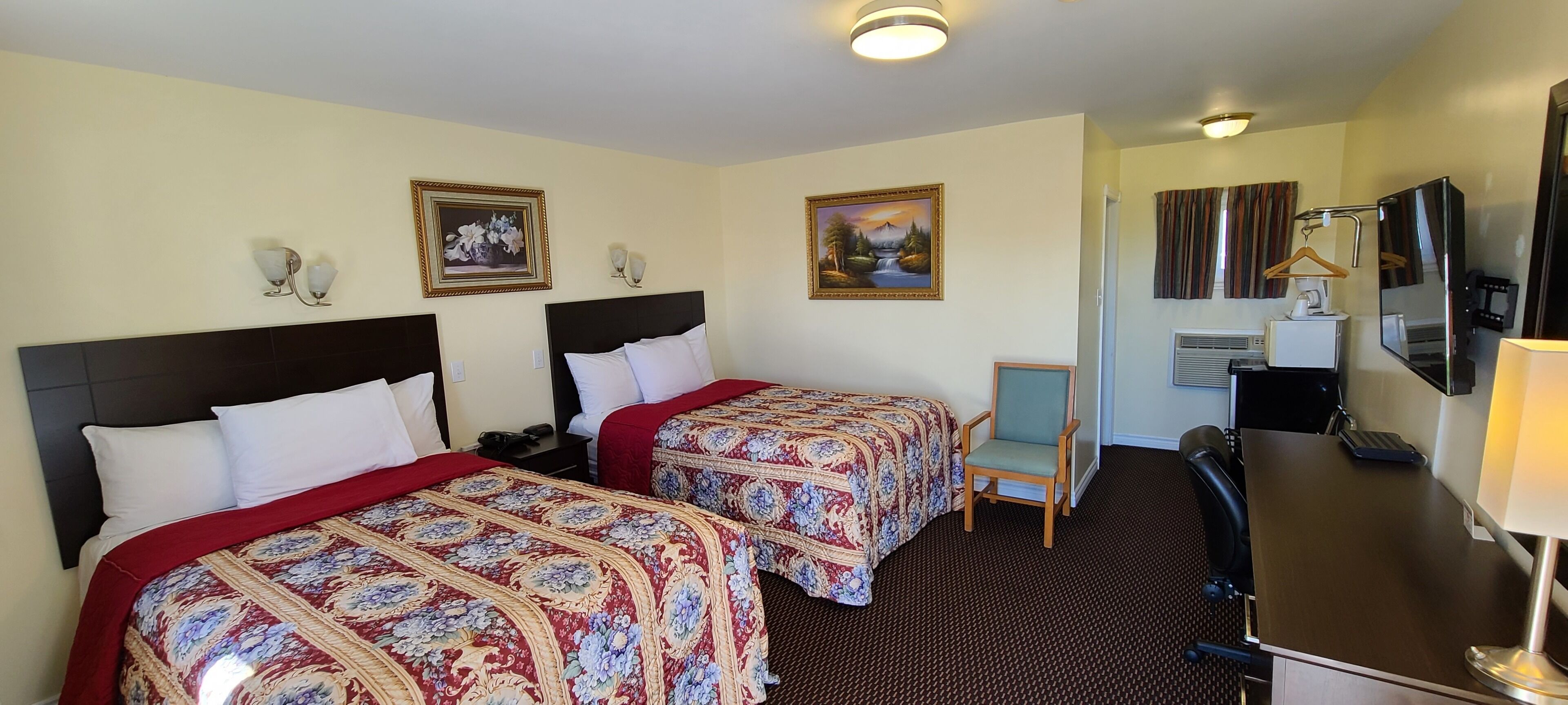 A hotel room with two beds, a desk, a chair, a TV, and a painting on the wall.